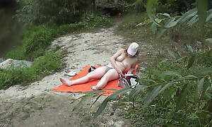 Wild beach. Random passerby guy peeps on sunbathing topless beautiful Milf on the river bank Outdoors. Outside. Naked in